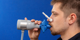 A man with a peg on his nose breathing into a breath measurer